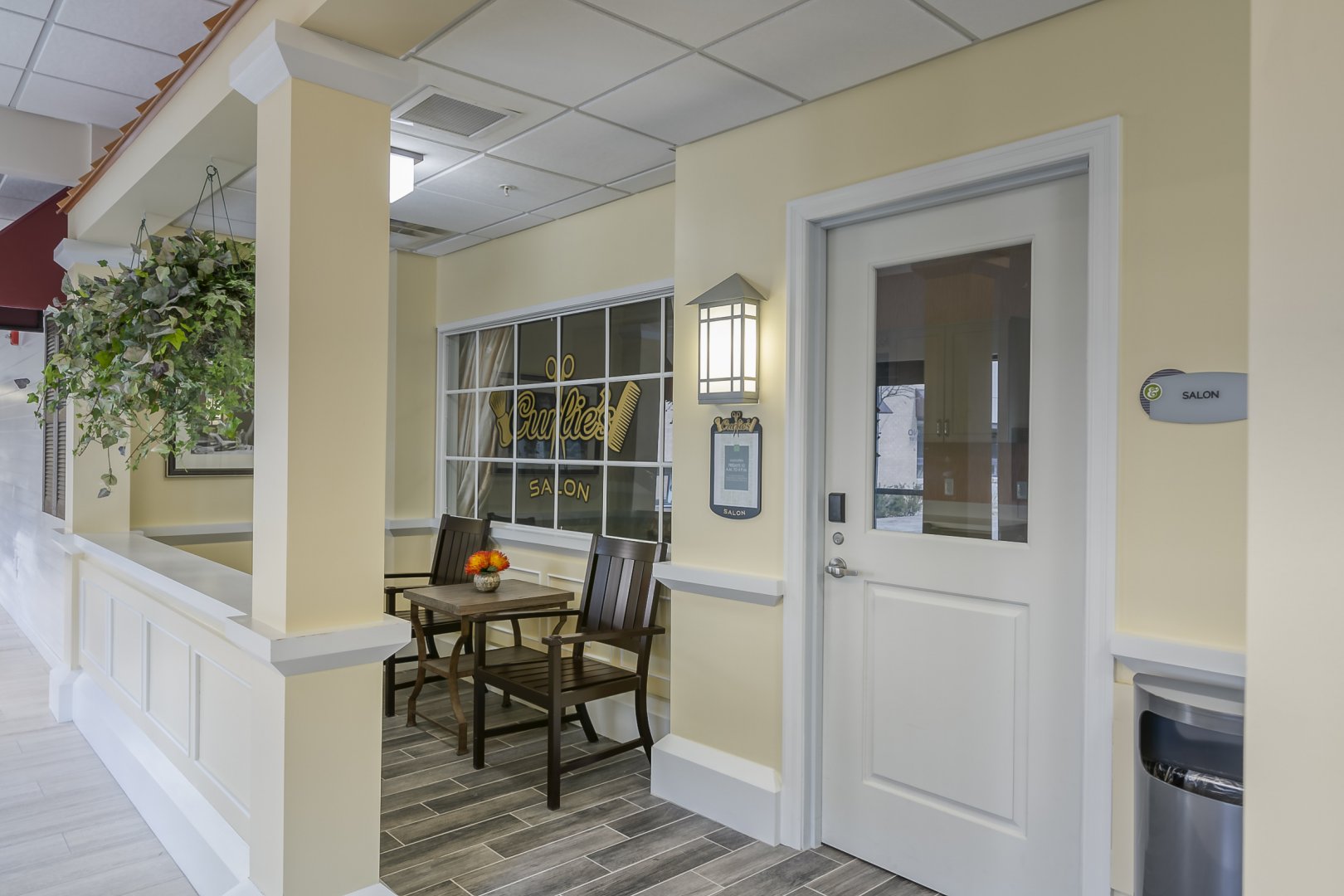 Welcoming Salon Entrance with Seating and Hanging Plant Welcoming entrance of a salon with chairs, table, and hanging plant in a bright, inviting setting.