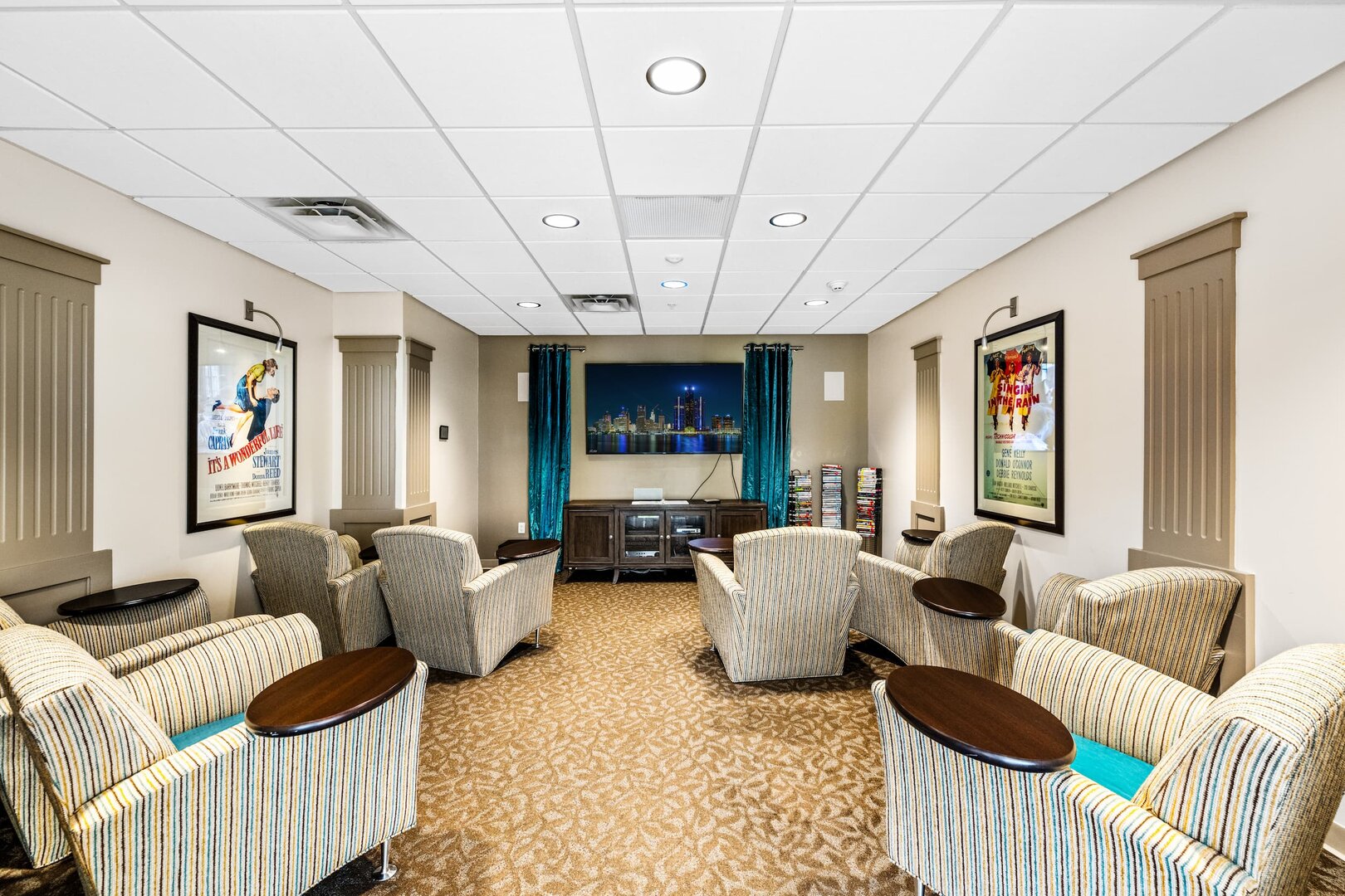 comfortable-media-room-senior-living Comfortable media room with striped chairs and a large wall-mounted TV in a senior living unit.